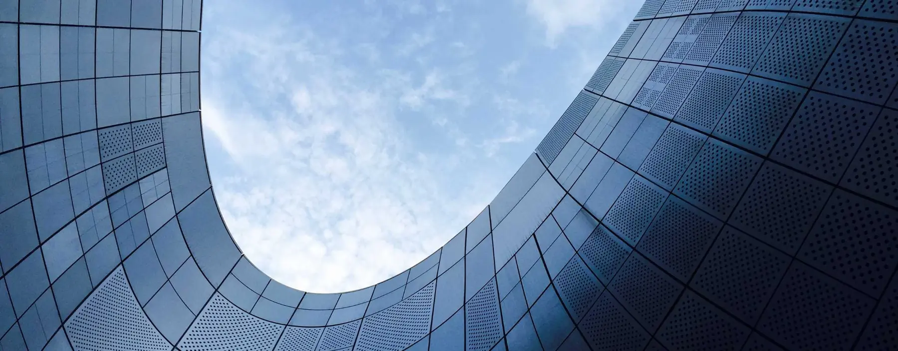 Curved glass and steel building facade under a blue sky