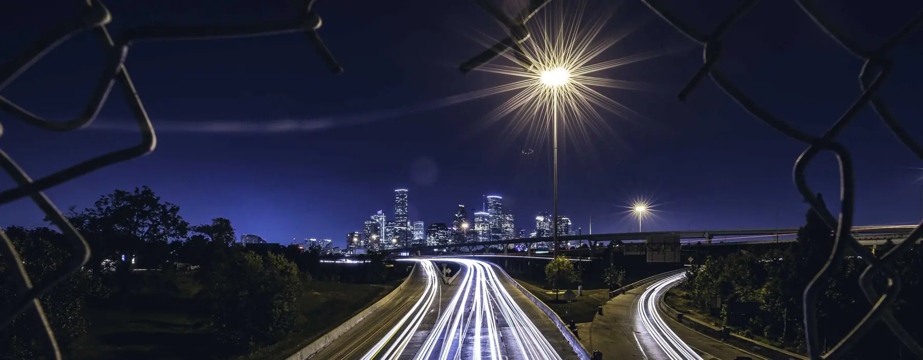 Highway light trails leading to a city skyline at night