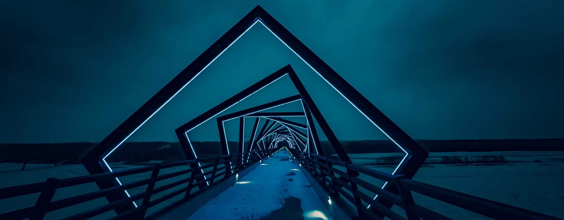 Geometric steel footbridge receding over water at dusk