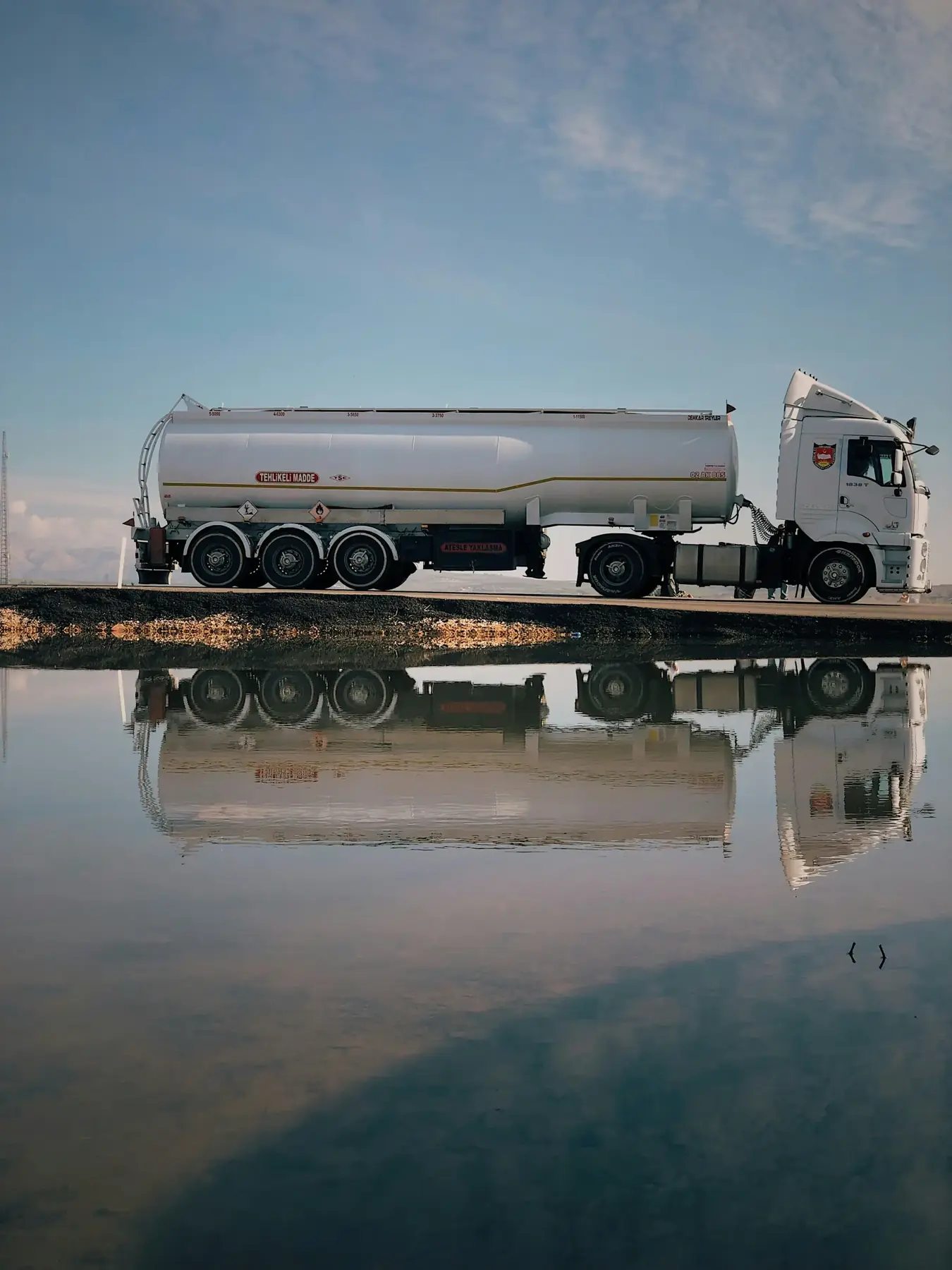 Fuel tanker truck on a flat road reflected in water